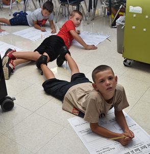 3 students writing on posters on floor